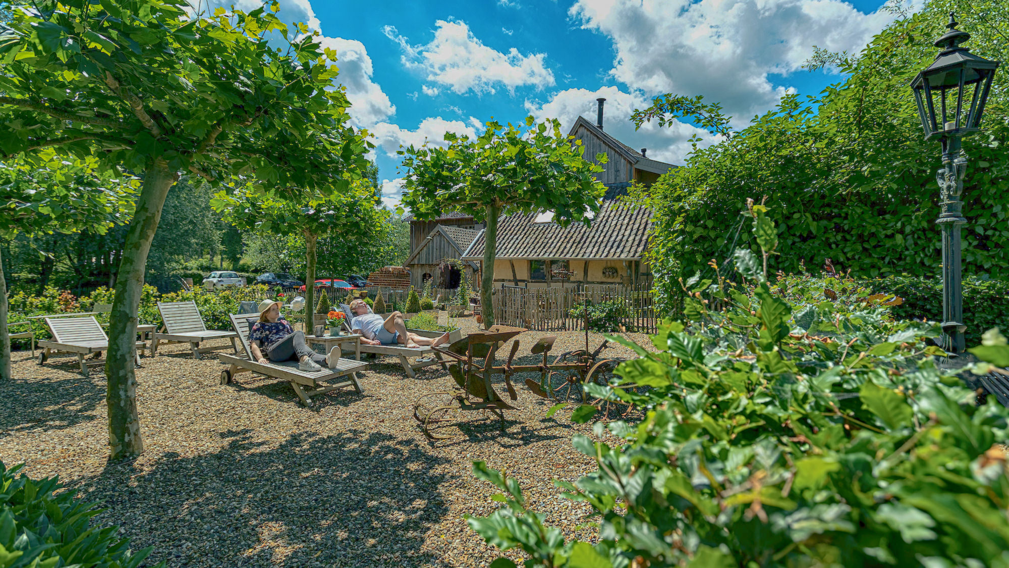 Gasten genieten op een ligbed in de tuin van Hoeve de witte Gans die aan het einde zichtbaar is.