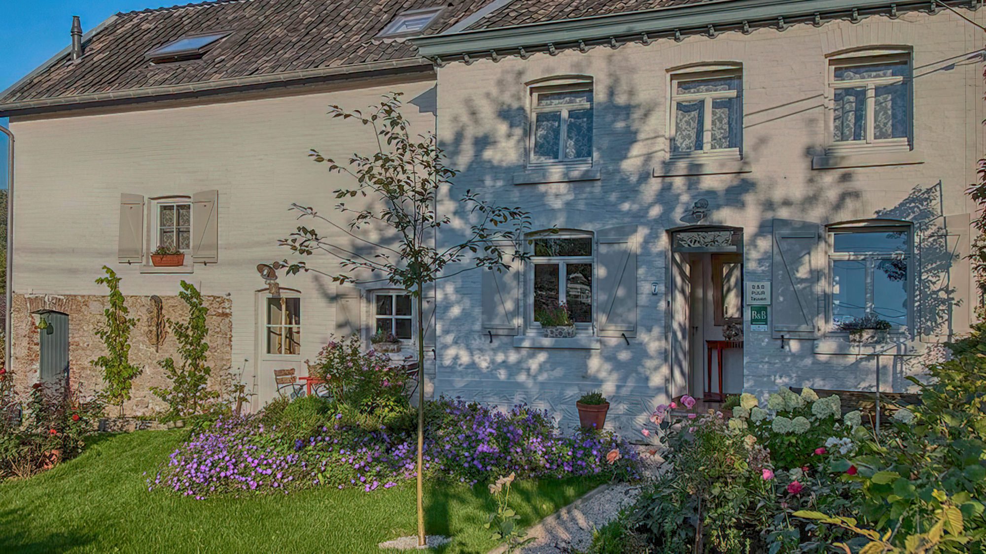 Die Fassade von Puur Teuven mit vielen bunten Blumen und Garten.